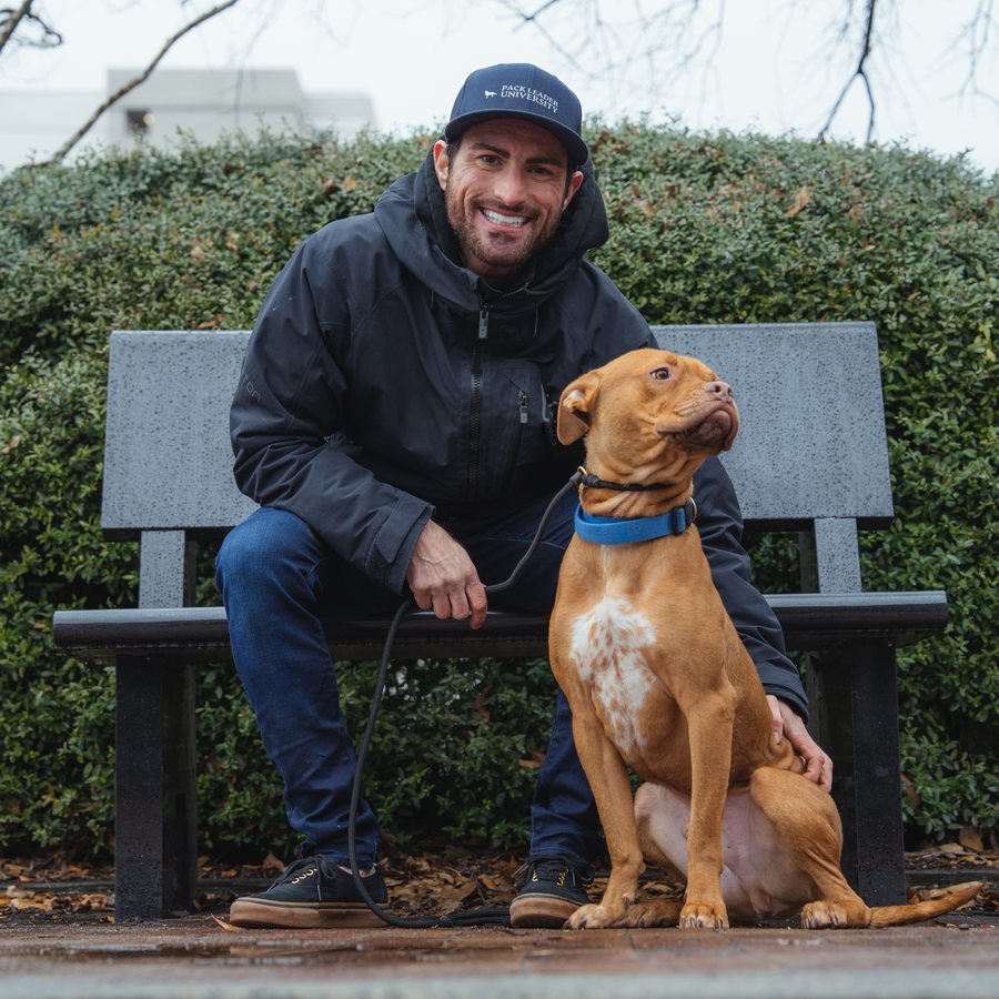 Ridge Vogel sitting on a bench, leaning forward with his hand resting on his dog&rsquo;s back